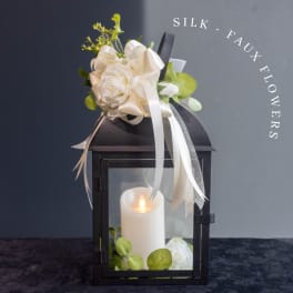 Black lantern with a white candle and cream silk flowers on top