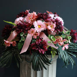 Pink and burgundy floral arrangement with ribbon on a pedestal