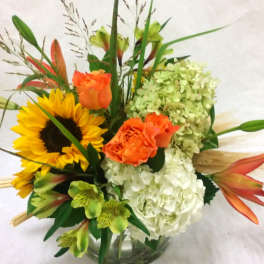 Bouquet with sunflowers, orange roses, white hydrangeas, and lilies in a glass vase