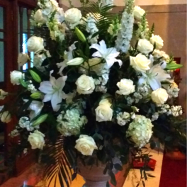 Large white floral arrangement in a pedestal vase with lilies and roses
