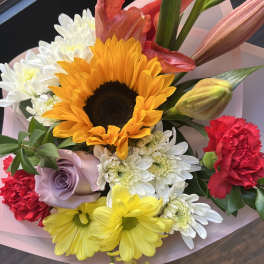 Bright mixed bouquet with sunflower, lilies, carnations, roses and daisies wrapped in pink paper