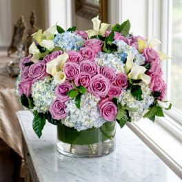 Pink roses, blue hydrangeas, and white calla lilies in a glass vase