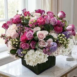 Pink and lavender rose arrangement in a dark square vase with white hydrangeas
