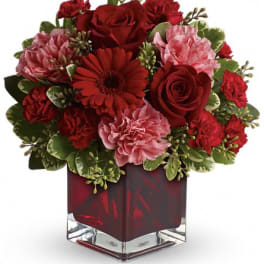 Red and pink flower arrangement in a square glass vase