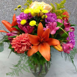 Colorful bouquet with orange lilies, pink flowers, and yellow blooms in a glass vase