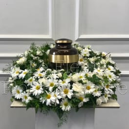 White daisy wreath around a dark urn with gold accents
