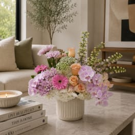 Pastel floral arrangement in a white vase with orchids, roses, and chrysanthemums