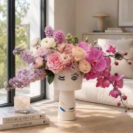 Pink and lavender floral arrangement in a face-shaped vase on a table