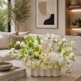 White and green floral arrangement in a low white vase on a coffee table