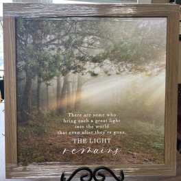 Framed memorial sign with a forest scene and the words "The light remains"