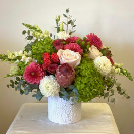 Mixed bouquet with roses, dahlias, hydrangeas, and a protea in a white vase