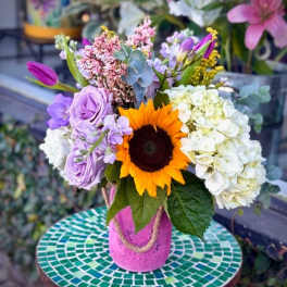 Mixed bouquet with a sunflower, lavender roses, and white hydrangeas in a pink vase
