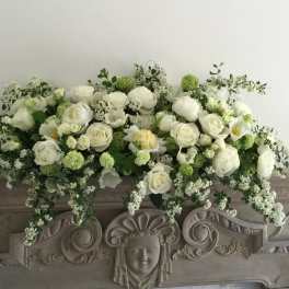 White floral arrangement with roses and peonies on an ornate mantel