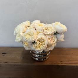 Cream roses arranged in a silver vase on a wooden table