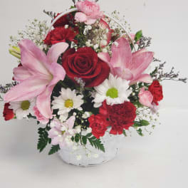 Basket arrangement of red roses, pink lilies, and white daisies