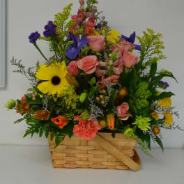 Mixed flower arrangement in a woven basket with pink, yellow, and purple blooms
