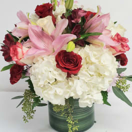 Bouquet of pink lilies, red roses, and white hydrangeas in a green vase