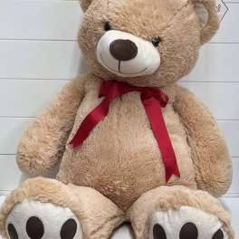 Large tan teddy bear with a red ribbon bow