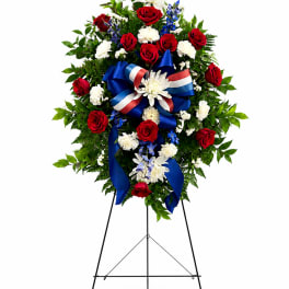 Standing floral wreath with red and white flowers and a blue ribbon on an easel