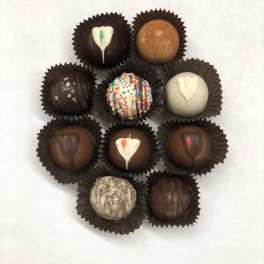 Assorted chocolate truffles with varied toppings arranged in a circle on a white background