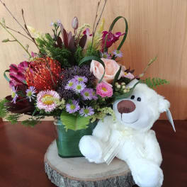 Mixed flower arrangement in a green vase with a white teddy bear