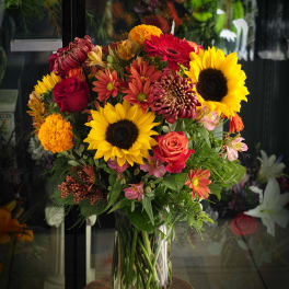 Mixed bouquet of sunflowers, roses, and chrysanthemums in a glass vase