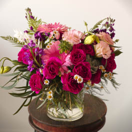 Pink and magenta bouquet with roses, gerbera daisies, and small white daisies in a glass vase