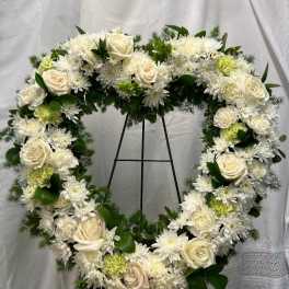 Heart-shaped white floral wreath on a black stand