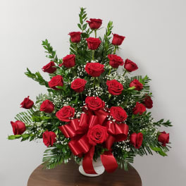 Red roses arranged in a white vase with a red ribbon