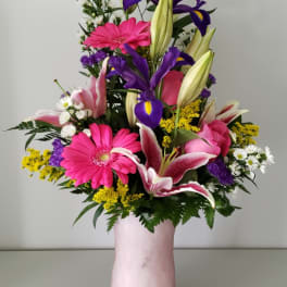 Mixed bouquet with pink gerberas, purple irises, and lilies in a pink vase