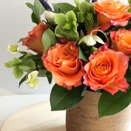 Orange roses in a tan vase with green and purple accents