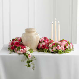 Pink rose arrangements around a beige urn with three candles
