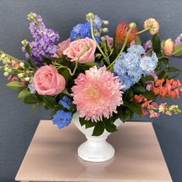 Mixed bouquet of pink roses, blue hydrangeas, and purple blooms in a white vase