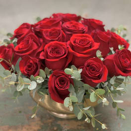 Red roses arranged in a gold bowl with eucalyptus accents