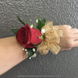 Red rose wrist corsage with gold ribbon on an arm