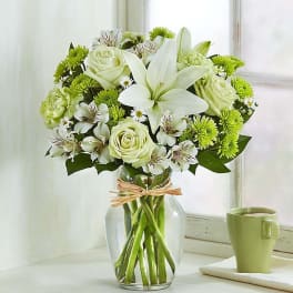 White lilies and roses in a clear glass vase with green mums