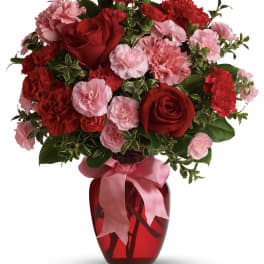 Red roses and pink carnations in a red glass vase with a pink ribbon