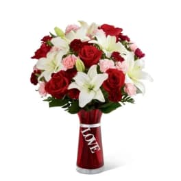Red roses, white lilies, and pink carnations in a red vase with a LOVE ribbon