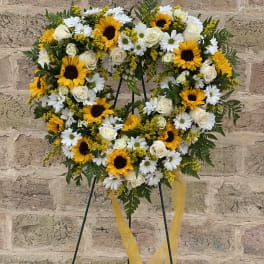 Heart-shaped floral wreath with sunflowers, white roses, and daisies on a stand