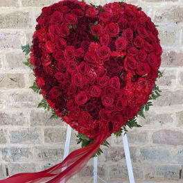 Heart-shaped red rose arrangement on a stand with a flowing ribbon