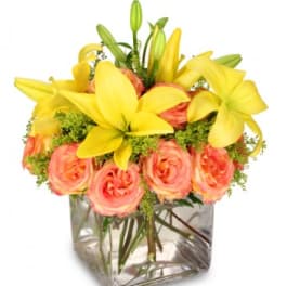 Yellow lilies and peach roses in a clear square vase
