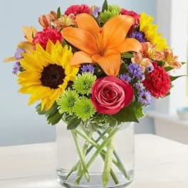 Colorful bouquet with sunflowers, lilies, and roses in a clear glass vase