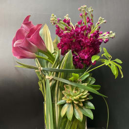 Pink calla lilies and magenta flowers in a clear glass vase