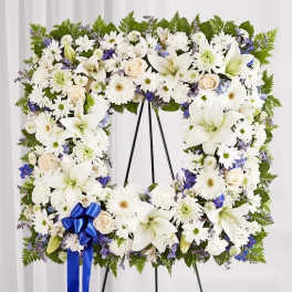 White floral wreath on a black easel with a blue ribbon bow