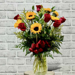 Red roses and yellow sunflowers in a glass vase with a red ribbon