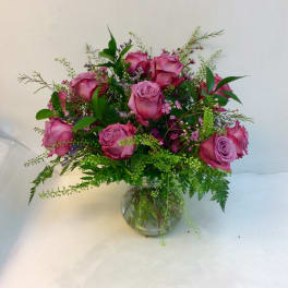 Pink roses arranged in a clear glass vase with mixed greenery