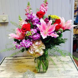 Mixed bouquet of pink lilies, red roses, and purple flowers in a glass vase