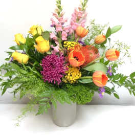 Mixed bouquet of yellow roses, orange tulips, and purple blooms in a vase