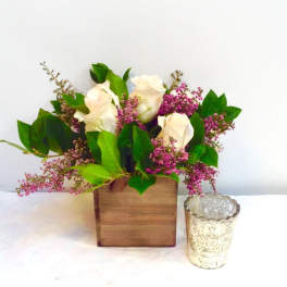 White roses and pink filler flowers in a wooden box with a glass votive beside it