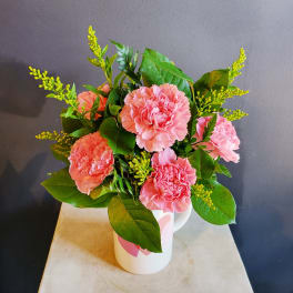 Pink carnations arranged in a white mug with green foliage